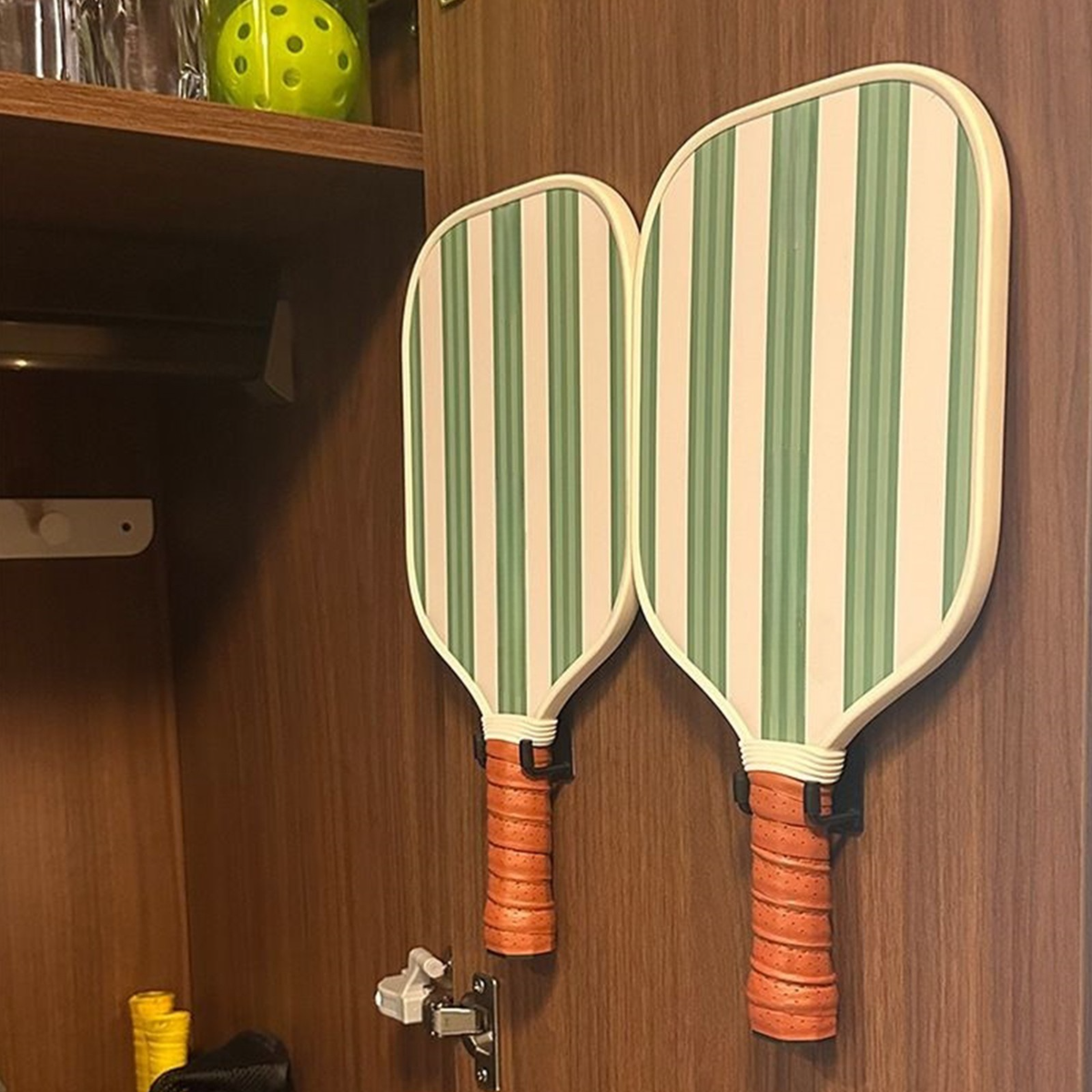 Two striped pickleball paddles hanging on a wooden door.