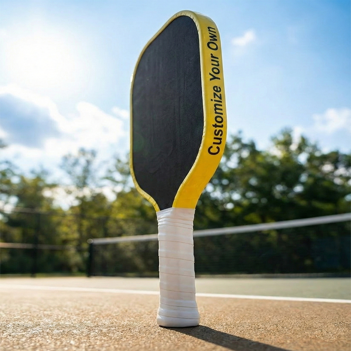 Pickleball paddle with 'Customize Your Own' text on a court with trees and sky in the background