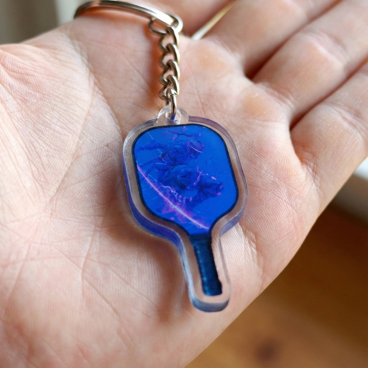 Blue pickleball paddle keychain held in a hand